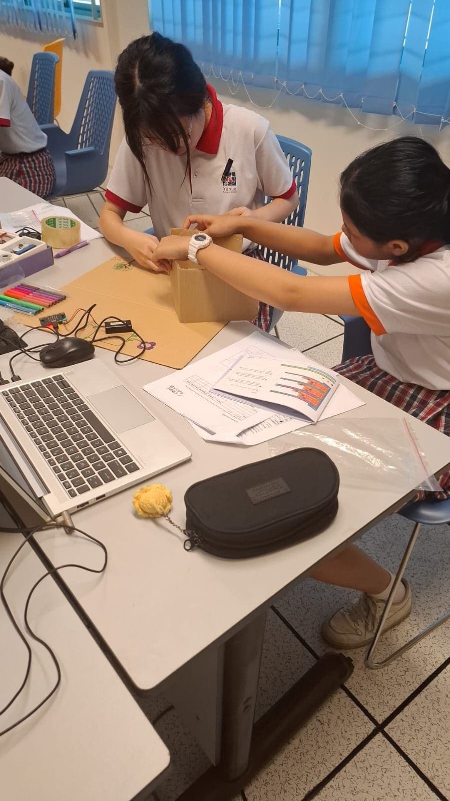 Two students taping together a cardboard prototype housing during a build