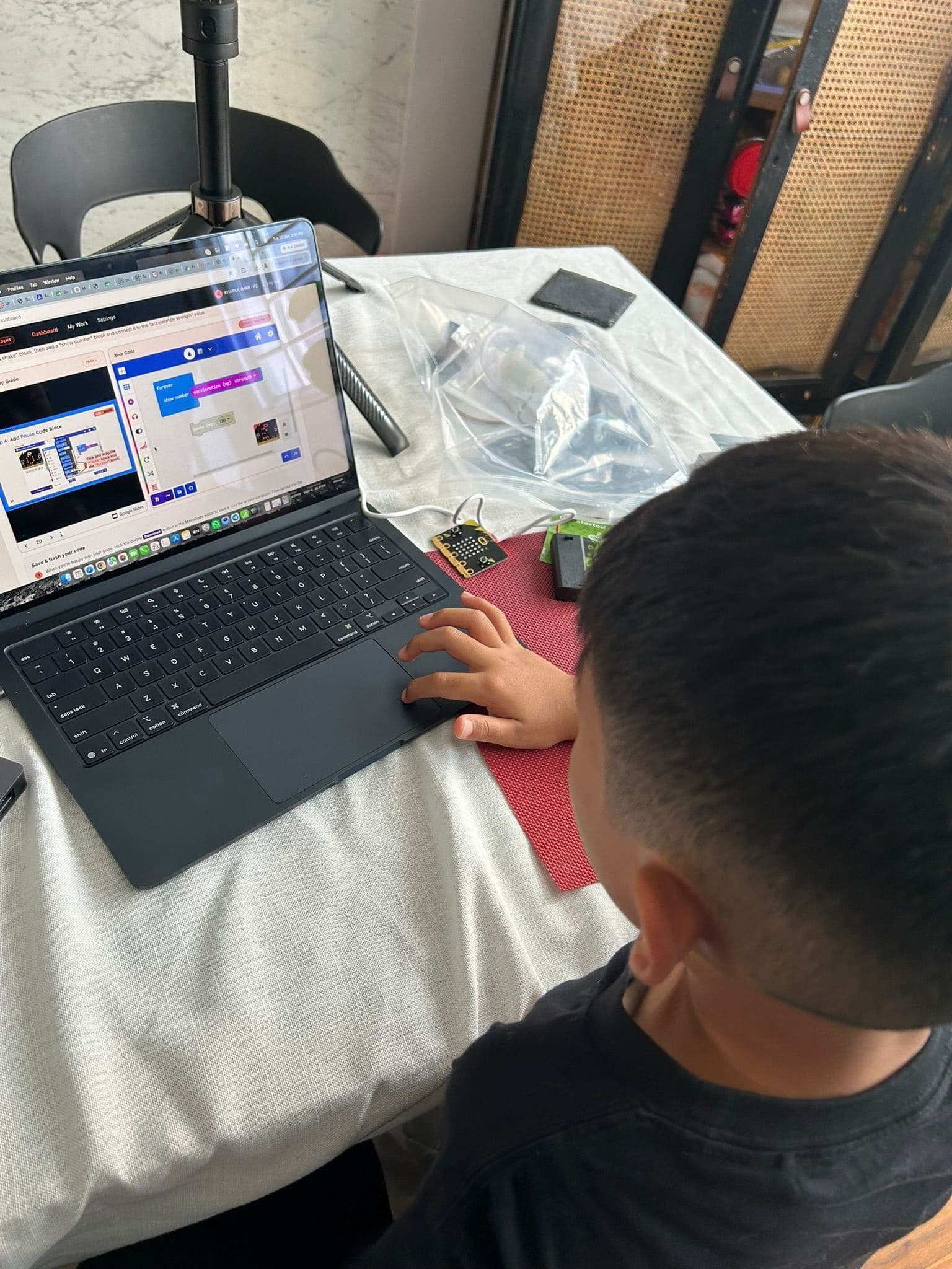 A child at a dining table with a laptop showing a lesson, a micro:bit and a component kit