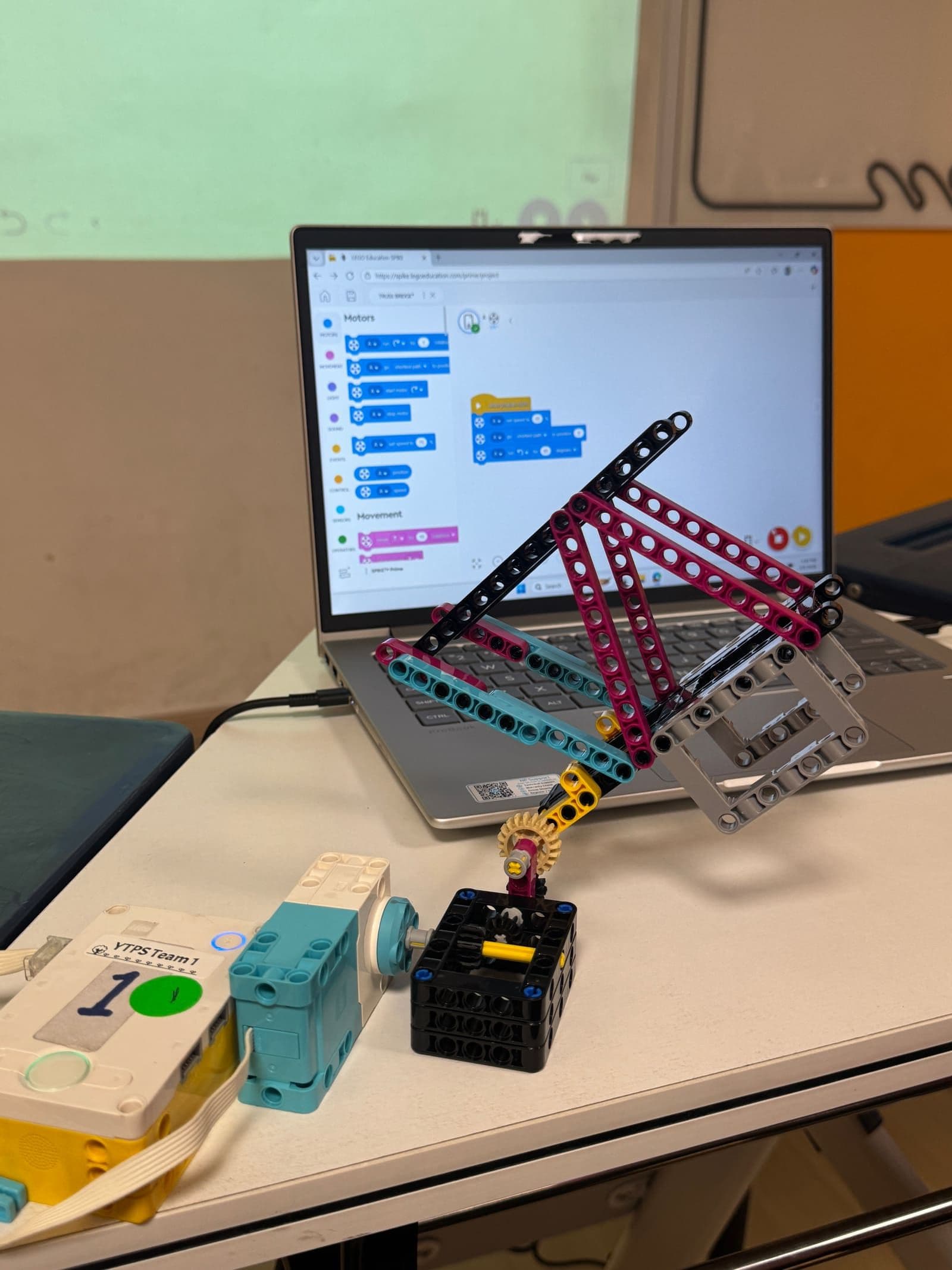 A SPIKE Prime robot arm beside a laptop showing the block programming editor
