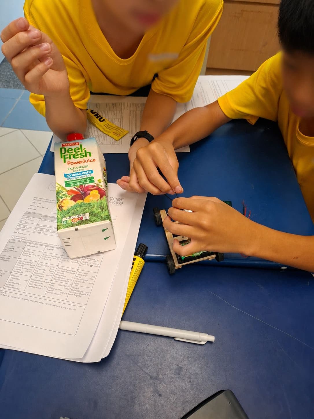 Two students wiring a motor into a chassis built from a juice carton